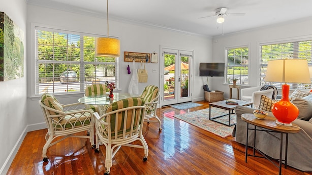 A spacious living room with a wooden floor, a glass table, wicker chairs, a sofa, and a TV.