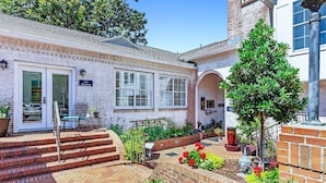 A brick building with a white door, a bench, and a small garden with flowers and a tree.