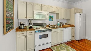A kitchen with white cabinets, a microwave, stove, and refrigerator. There is a chalkboard with writing on the wall.