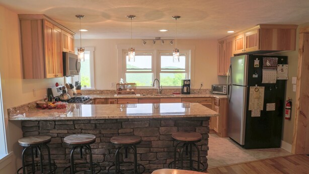 A kitchen with a stone island, wooden bar stools, a refrigerator, and a window with a view. - Hidden Ridge - A quiet mountain area (Bellefonte)