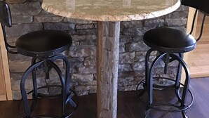 A round table with two black barstools, a stone wall, and a clock on the wall. - Hidden Ridge - A quiet mountain area (Bellefonte)