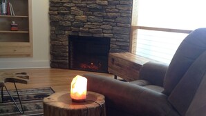 A cozy living room with a stone fireplace, a wooden coffee table with a candle, and a leather sofa. - Hidden Ridge - A quiet mountain area (Bellefonte)