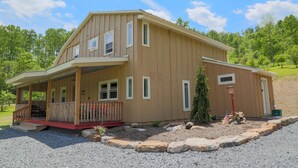 A two-story wooden house with a porch, a small deck, and a front yard with rocks and a tree. - Hidden Ridge - A quiet mountain area (Bellefonte)