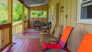 A porch with wooden chairs and a table, a window with a view of greenery, and a door with a sign. - Hidden Ridge - A quiet mountain area (Bellefonte)