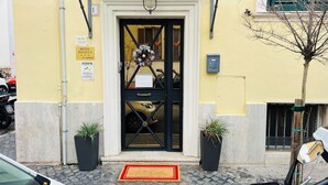 L’entrée d’un hôtel, avec une porte noire, un paillasson et deux plantes en pot.