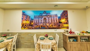 Un coin repas agrémenté d’une grande fresque représentant un bâtiment historique, d’un buffet en bois contenant de l’ustensile de cuisine et d’une table dressée pour deux personnes.