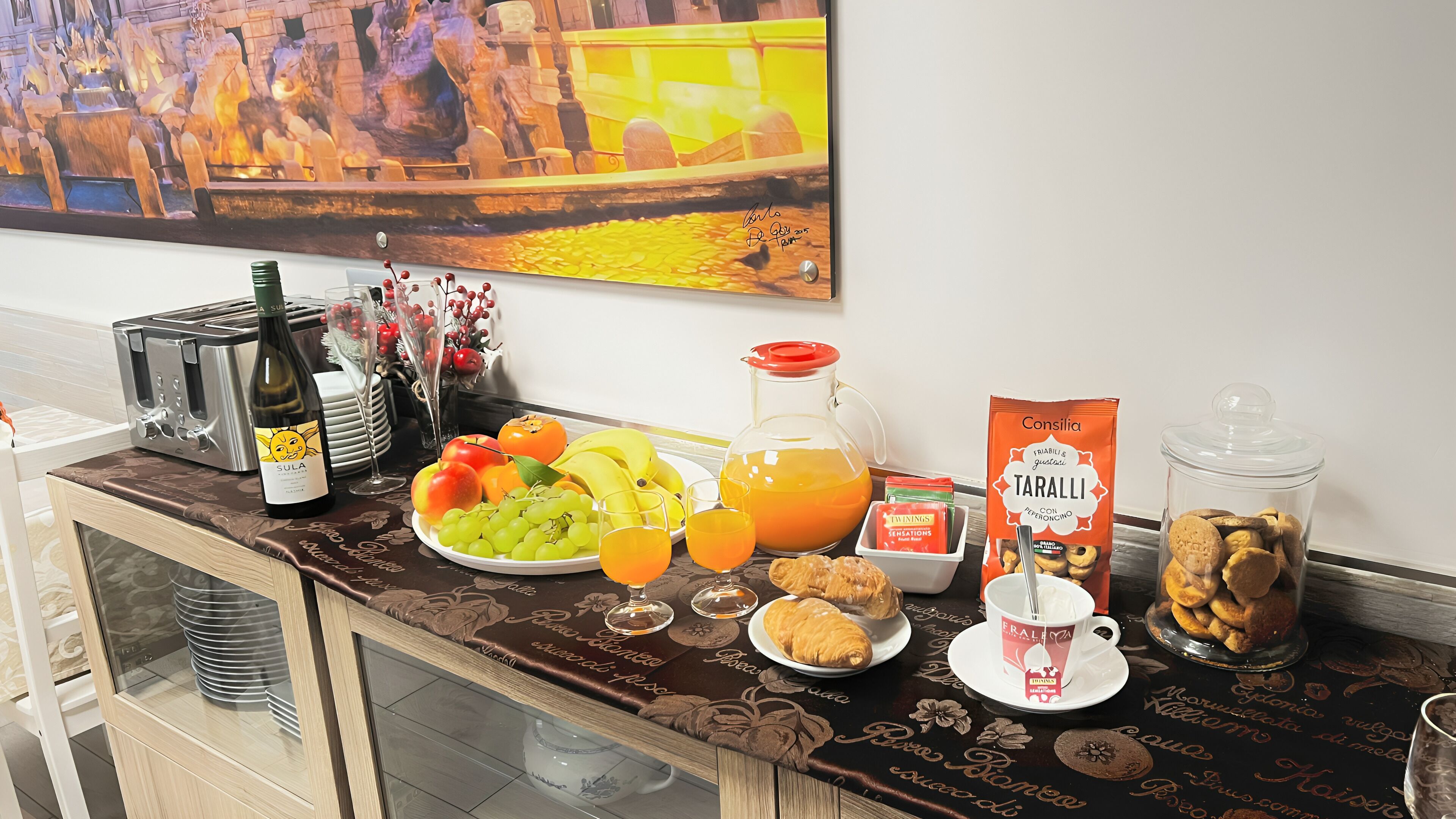 A breakfast buffet with various food items, a wine bottle, and a decorative painting on the wall.