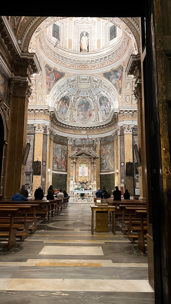An interior of a church with ornate ceilings, a central altar, and pews arranged for seating. - Hotel Balilla (Rome)