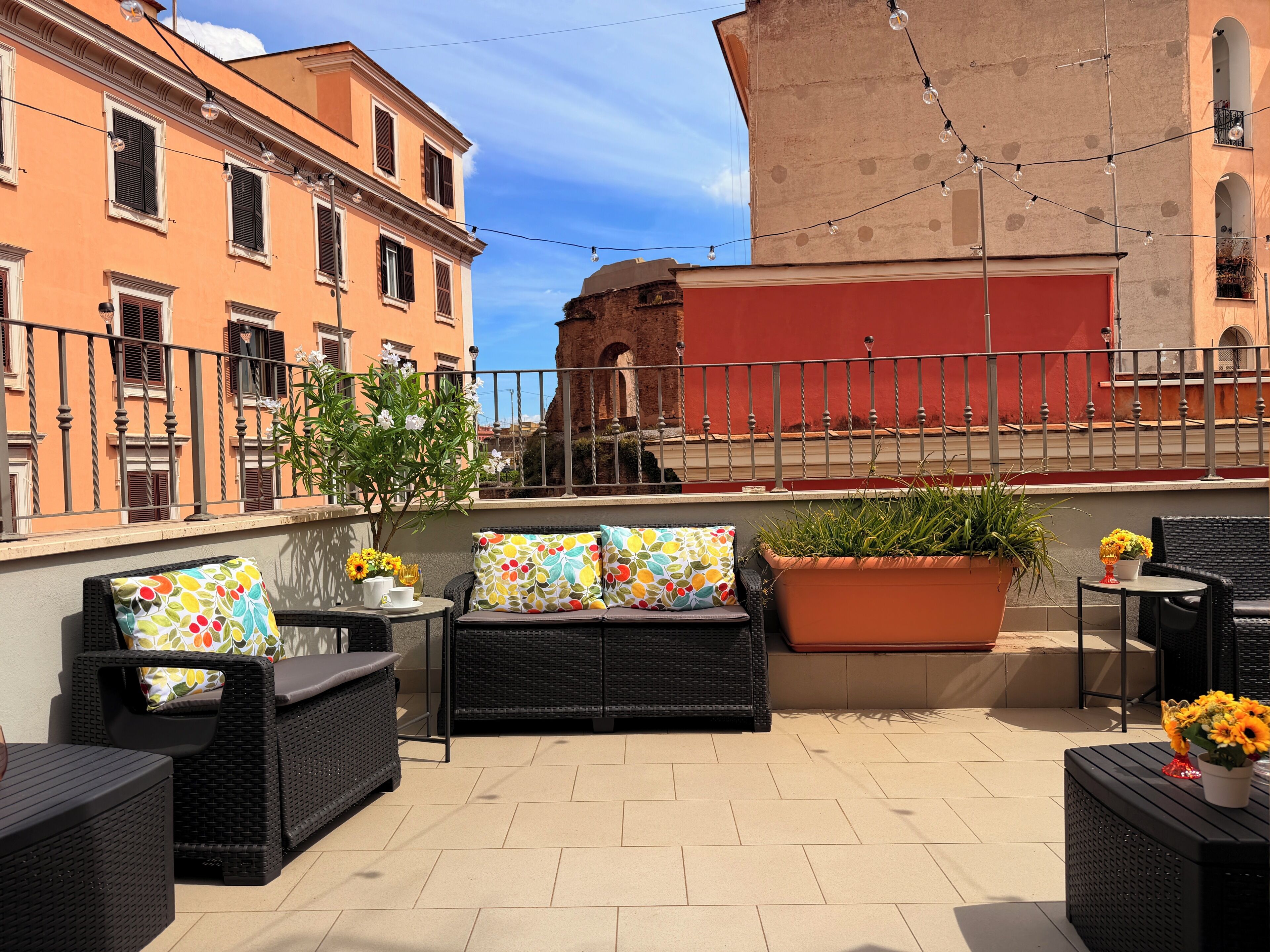 Un espacio al aire libre con mobiliario de mimbre, una planta en maceta y vistas a edificios históricos.