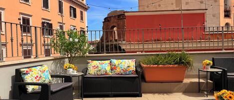 Un espacio al aire libre con mobiliario de mimbre, una planta en maceta y vistas a edificios históricos.