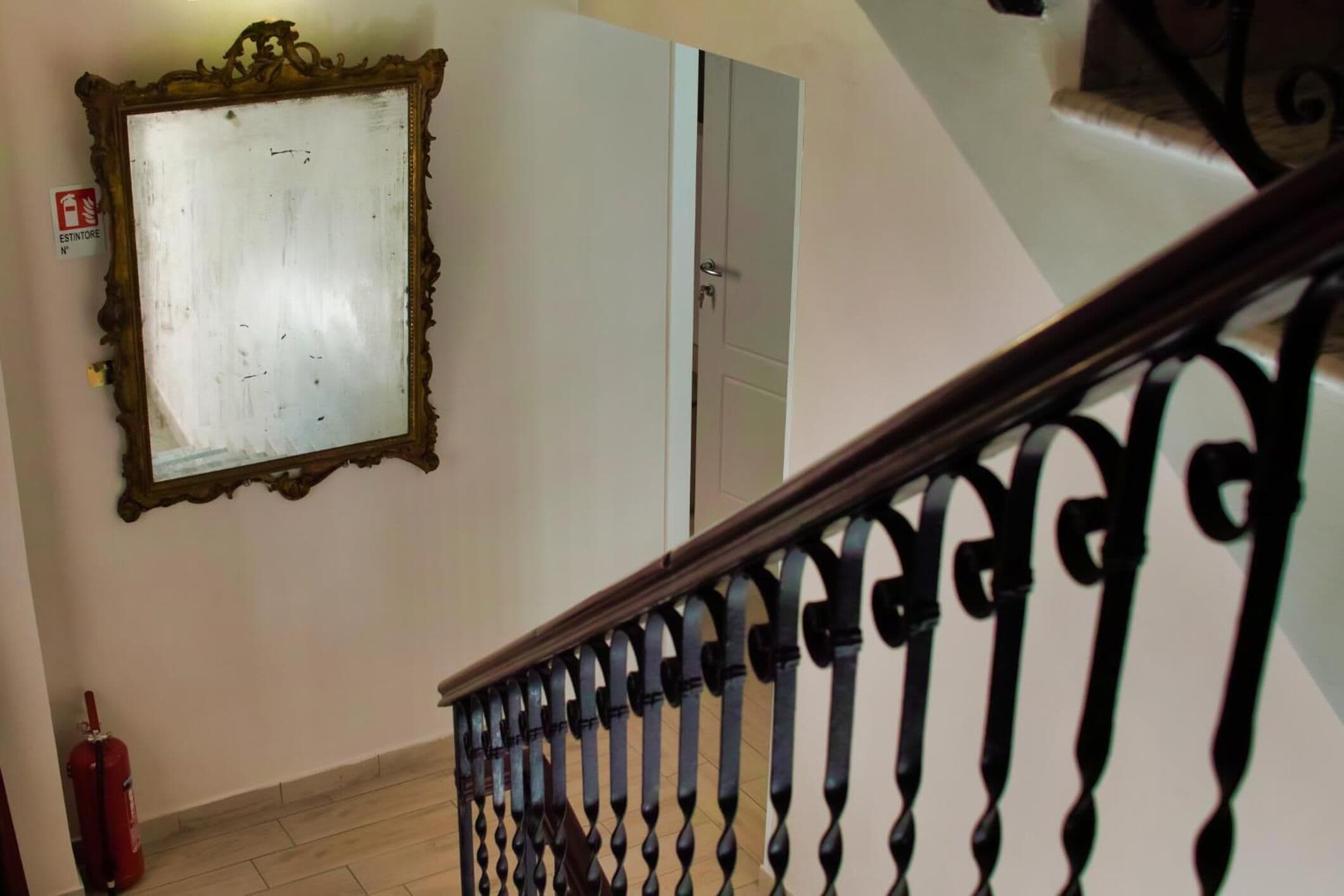 Een trap met een zwart ijzeren hekwerk, een witte deur en een spiegel met een decoratieve lijst.