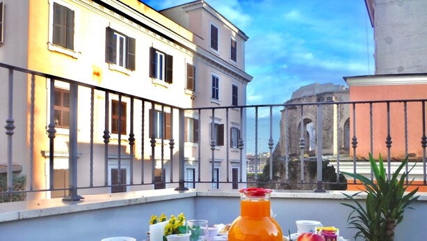 Un balcon avec une table préparée pour le petit-déjeuner, comprenant une carafe de jus d’orange, des fruits et des viennoiseries.