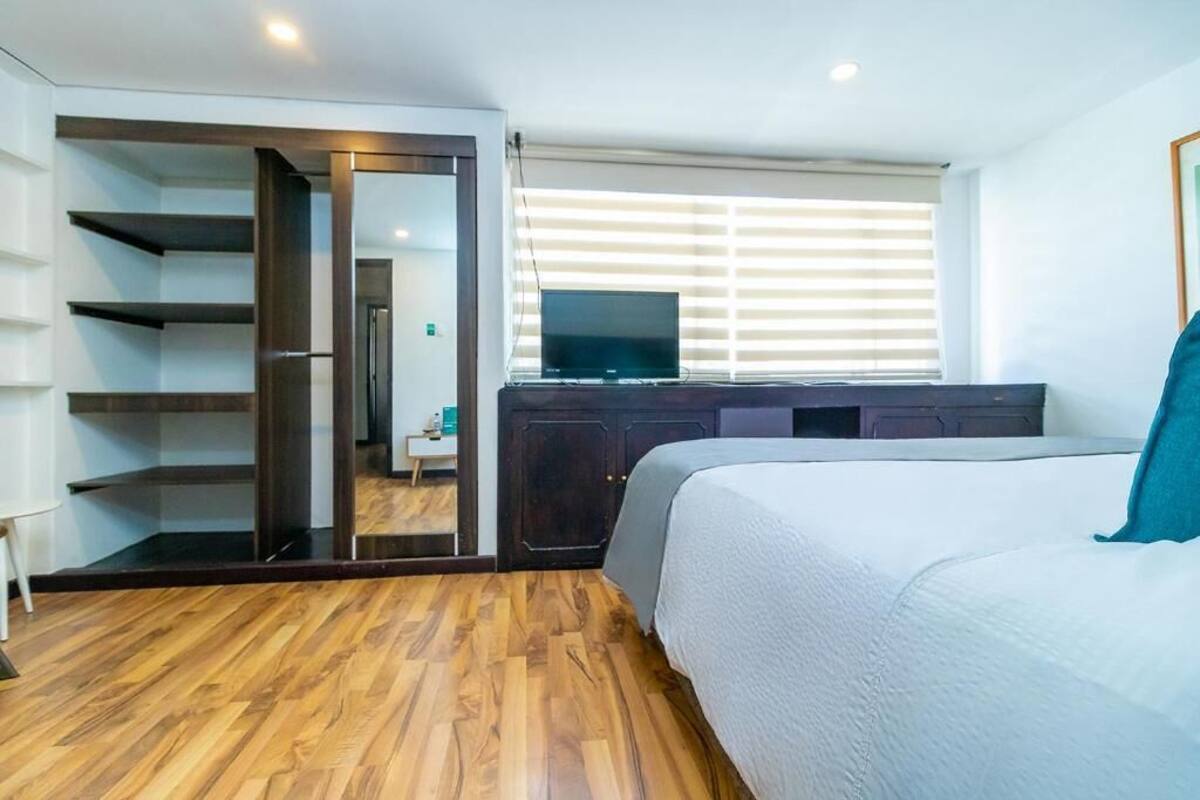 Un dormitorio con cama, televisor, armario y suelo de madera.