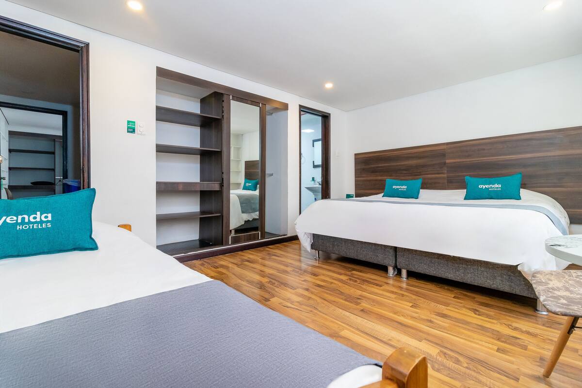 Una habitación de hotel con dos camas, un armario, un espejo y una pequeña mesa.