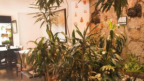 A room with a large indoor plant arrangement, a stone wall, and a dining area with tables and chairs. - Hotel Bogota Alpes Polo Club (Bogotá)