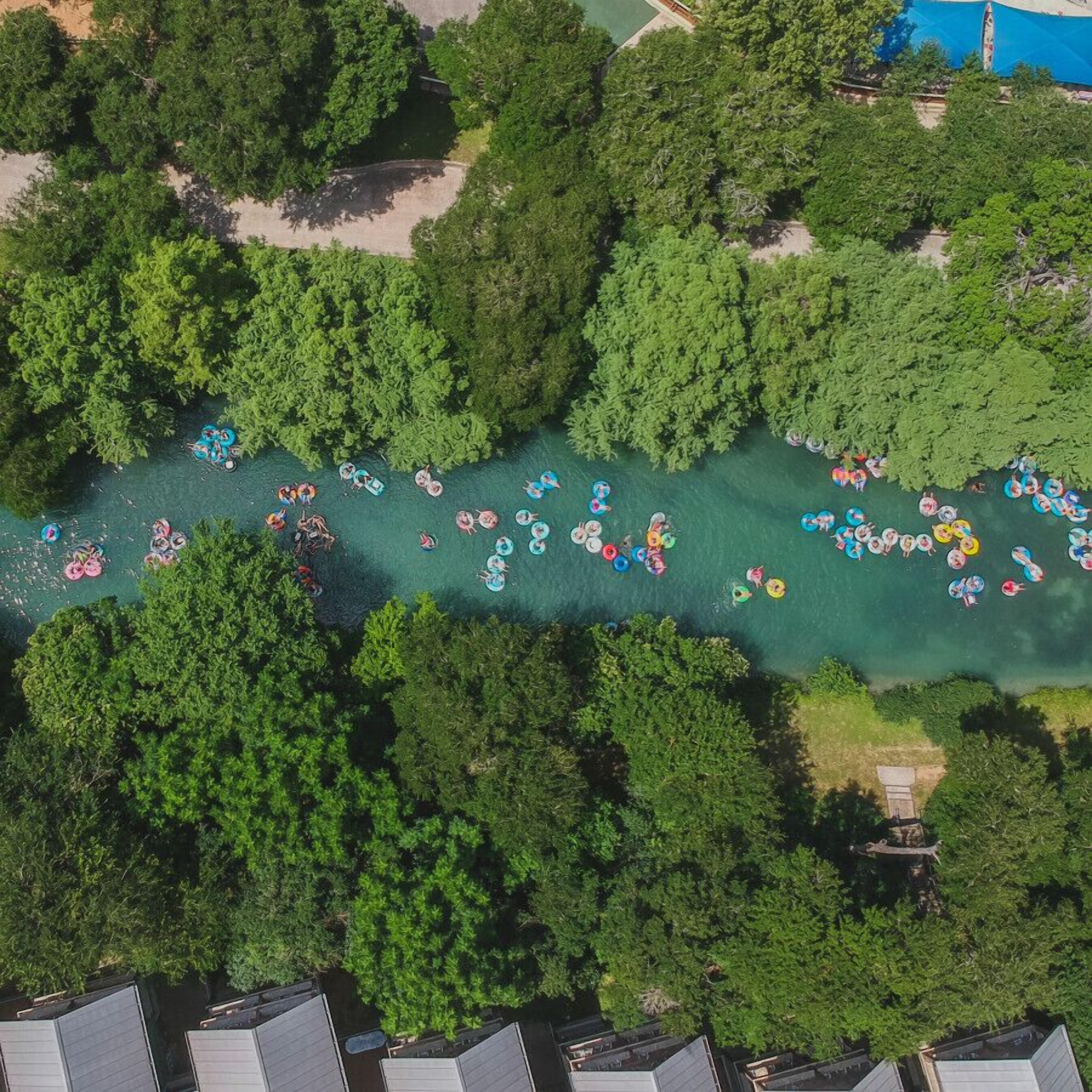 Vista aérea de un río con gente en flotadores, rodeado de abundante vegetación y edificios residenciales.