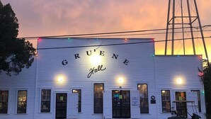 A building with 'GRUENE Hall' signage, a water tower, and a wet ground reflecting lights. - CRC331*Direct Comal River Access*Walk to Downtown NBTX (New Braunfels)