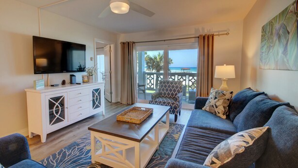 A modern living room with a flat-screen TV, a white cabinet, a sofa, a coffee table, and a view of the outdoors. - El Matador 427 - FREE TICKETS!! Your stay includes free tickets to many area attractions! (Fort Walton Beach)