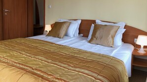 A hotel room with a bed, wooden headboard, two bedside tables with lamps, and a door. - Hotel Beatris (Nessebar)