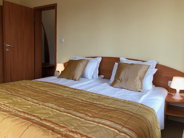 A hotel room with a bed, wooden headboard, two bedside tables with lamps, and a door.