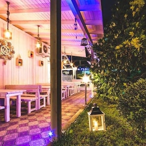 An outdoor seating area with wooden benches and tables, a pathway, and a sign for 'A PLUS'. - Hotel Beatris (Nessebar)