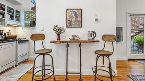 Una cocina con armarios blancos, una estufa y un comedor con dos taburetes y una mesa.