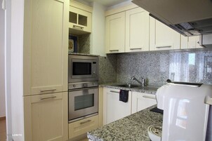 Una cucina compatta con pensili chiari, un forno a microonde, un forno, un lavello e un frigorifero bianco.