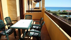 Een balkon met een tafel en stoelen, met uitzicht op een heldere blauwe zee en een zwembad.
