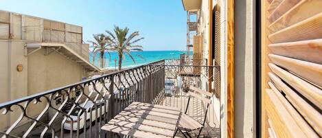 A balcony with a view of the sea, a palm tree, and a wooden fence.