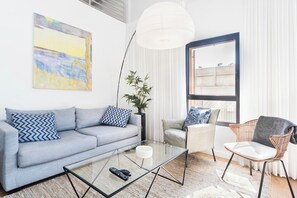 A modern living room with a sofa, armchair, glass coffee table, and a large window.