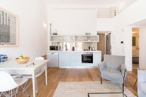 A modern kitchen with white cabinetry, a dining area with a white table and chairs, and a grey armchair.