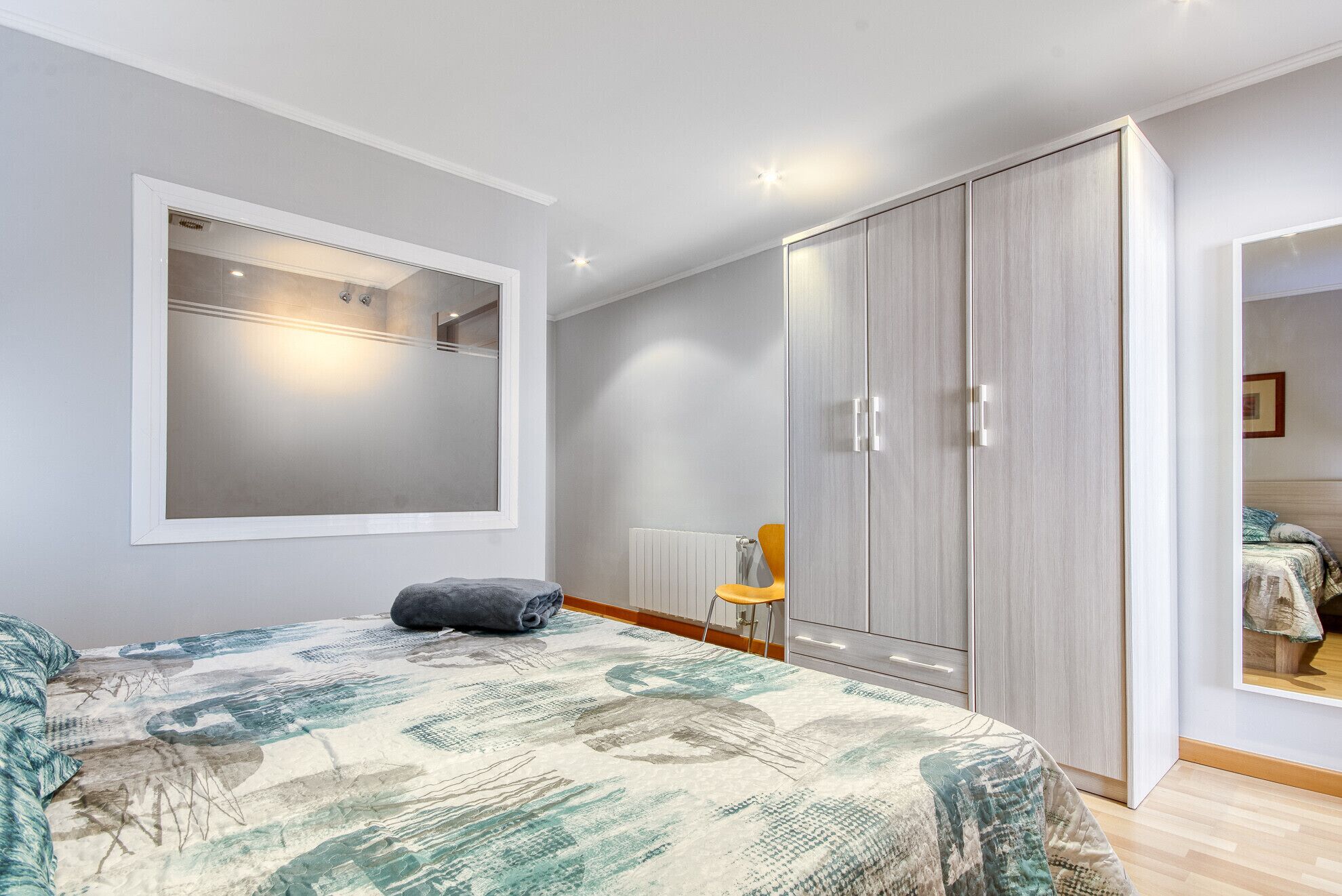 Een slaapkamer met een bed, een kledingkast, een spiegel en een raam.