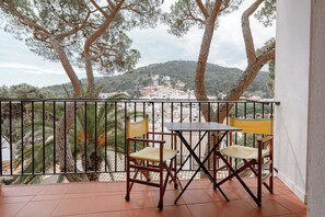 A balcony with two wooden chairs and a table, overlooking a town with buildings and trees.