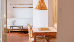 Une pièce comprenant un lit, une table à manger avec des chaises, un luminaire suspendu en osier et un mur blanc.