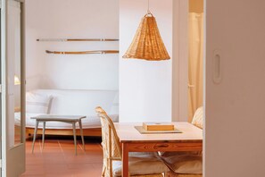 A room with a bed, a dining table with chairs, a hanging wicker light fixture, and a white wall.