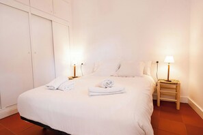 A neatly made bed with white linens and towels, two bedside lamps, and a wooden nightstand.