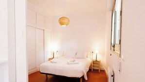 Une chambre à coucher comprenant un lit, des lampes de chevet, un luminaire suspendu, une armoire et un radiateur.