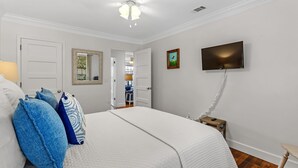 A bedroom with a bed, a TV, a mirror, and a door. - Cypress at Jubilee Suites Bed & Breakfast. 1K/1Q/1B (Fairhope)