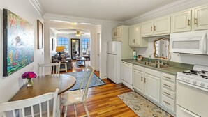 A modern kitchen with white cabinets, a stove, and a sink. There is a dining area with a table and chairs. - Cypress at Jubilee Suites Bed & Breakfast. 1K/1Q/1B (Fairhope)