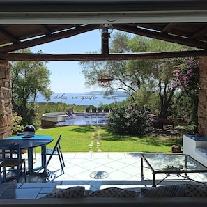 A covered patio with a view of a swimming pool and garden.