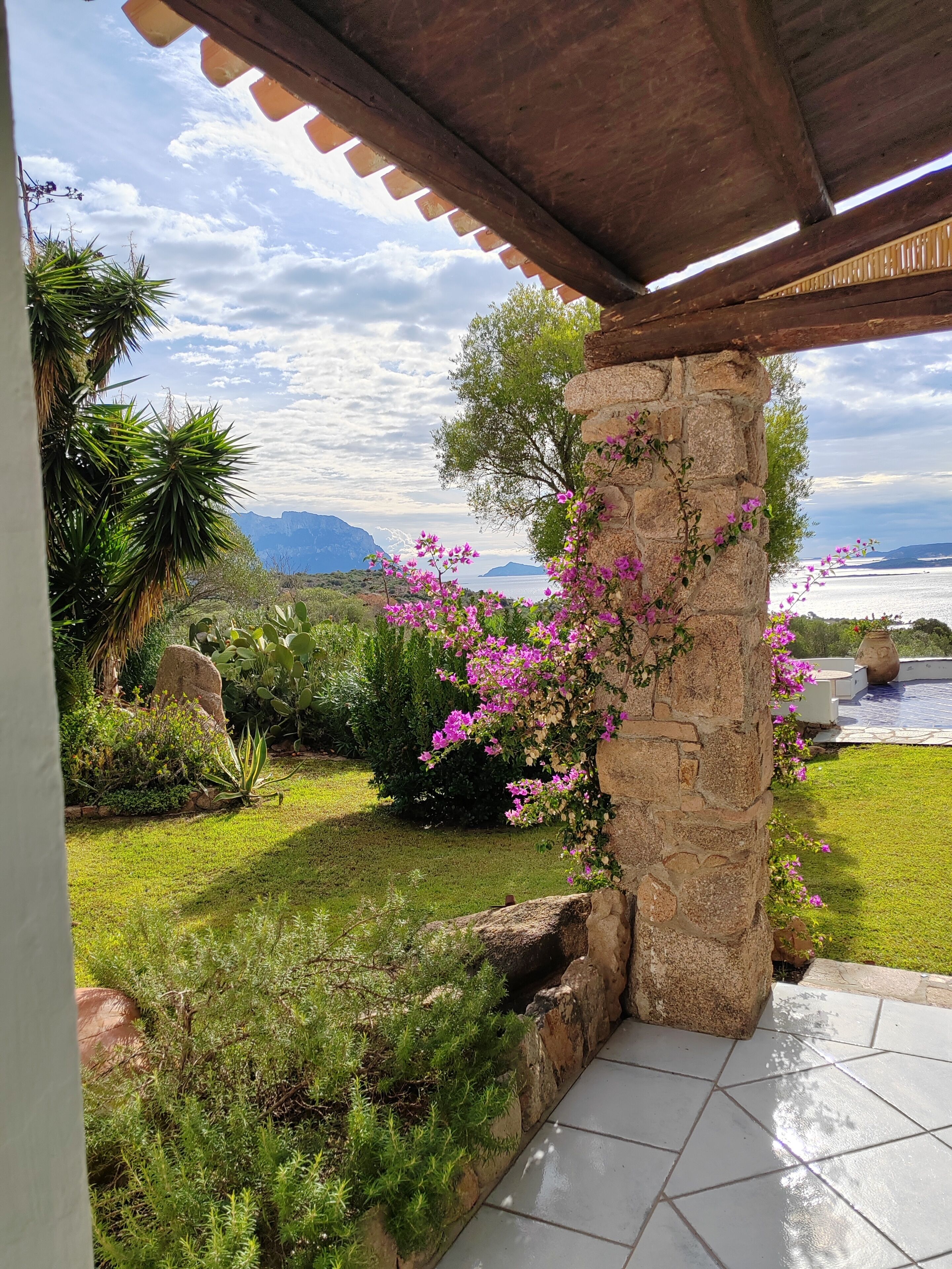 A garden with a stone pillar, a pool, and a view of the sea.