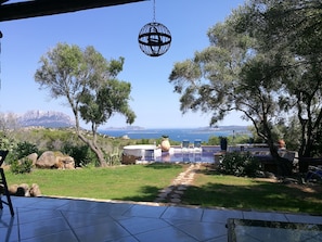 A patio with a view of the sea, outdoor seating, and a hanging light fixture.