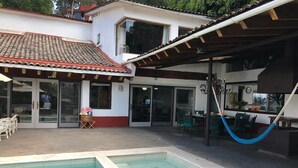 Una piscina con plataforma de baldosas, un porche cubierto y mobiliario exterior.