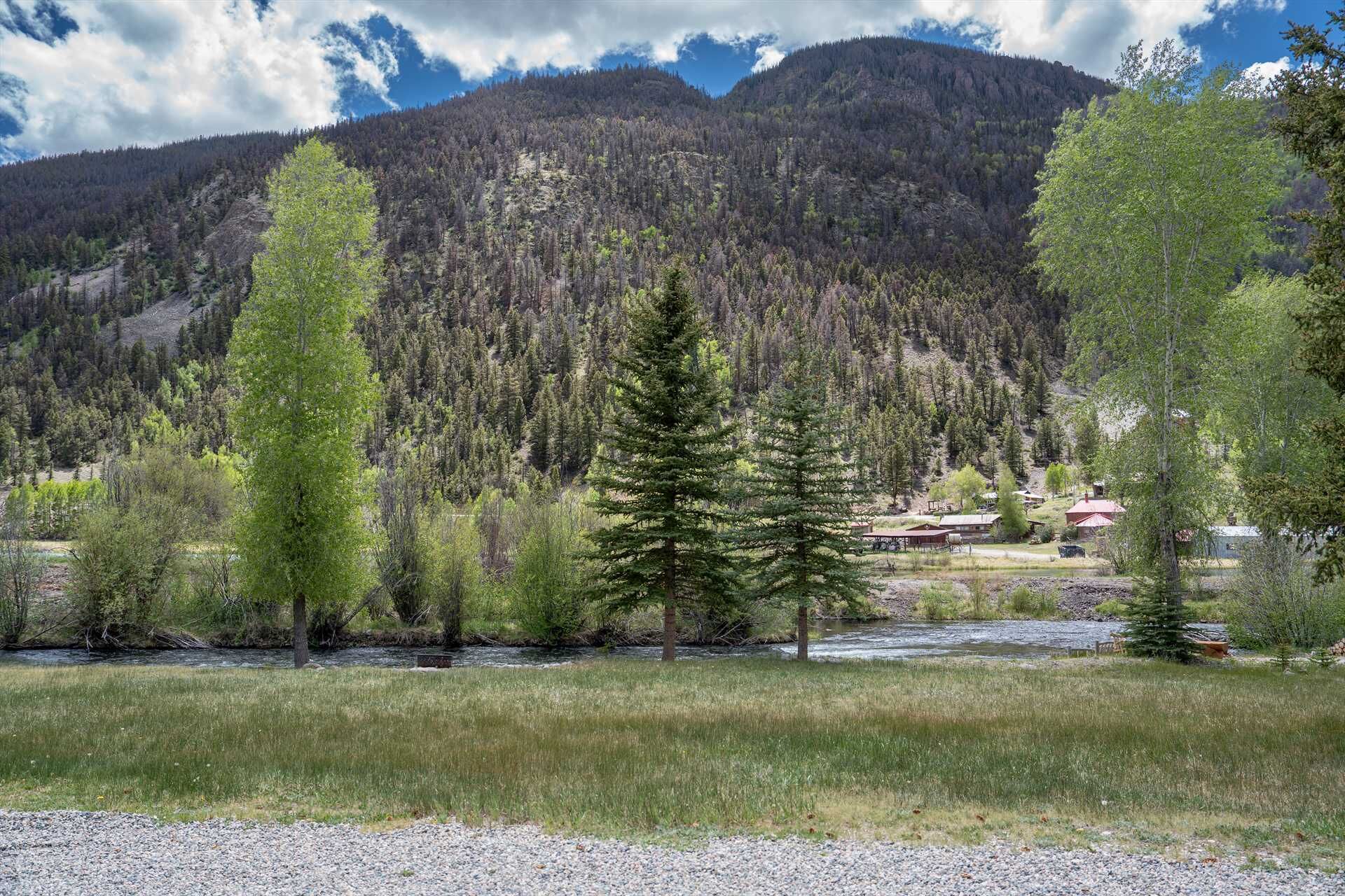 A rural landscape with a river, a mountain in the background, and a small settlement with buildings.