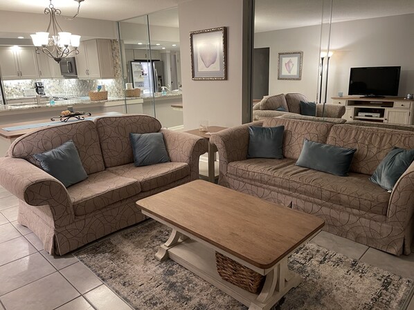 A modern living room with a sectional sofa, a wooden coffee table, and a large mirror reflecting the kitchen area. - Oceanfront Oasis (Myrtle Beach)