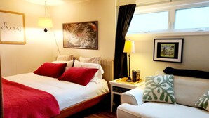Habitación de hotel con cama, sofá, mesita de noche, lámpara y ventana con cortinas.