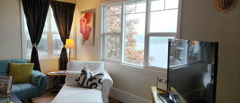 Una habitación acogedora con sofá, televisión, lámpara y ventana con vistas a árboles y una masa de agua.
