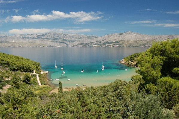 A coastal landscape with a clear view of a bay, boats, and distant mountains.