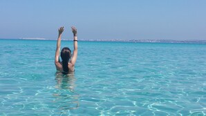Eine Person schwimmt in klarem, blauem Wasser, im Hintergrund ist eine Stadtlandschaft zu sehen.