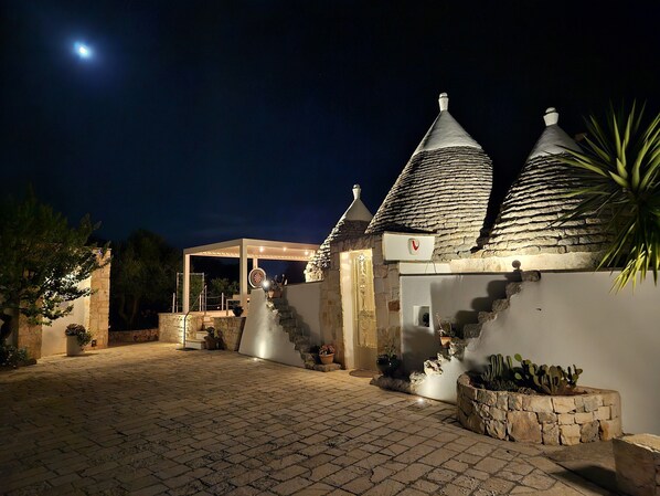 A courtyard with stone walls, a covered seating area, and a moonlit night sky.